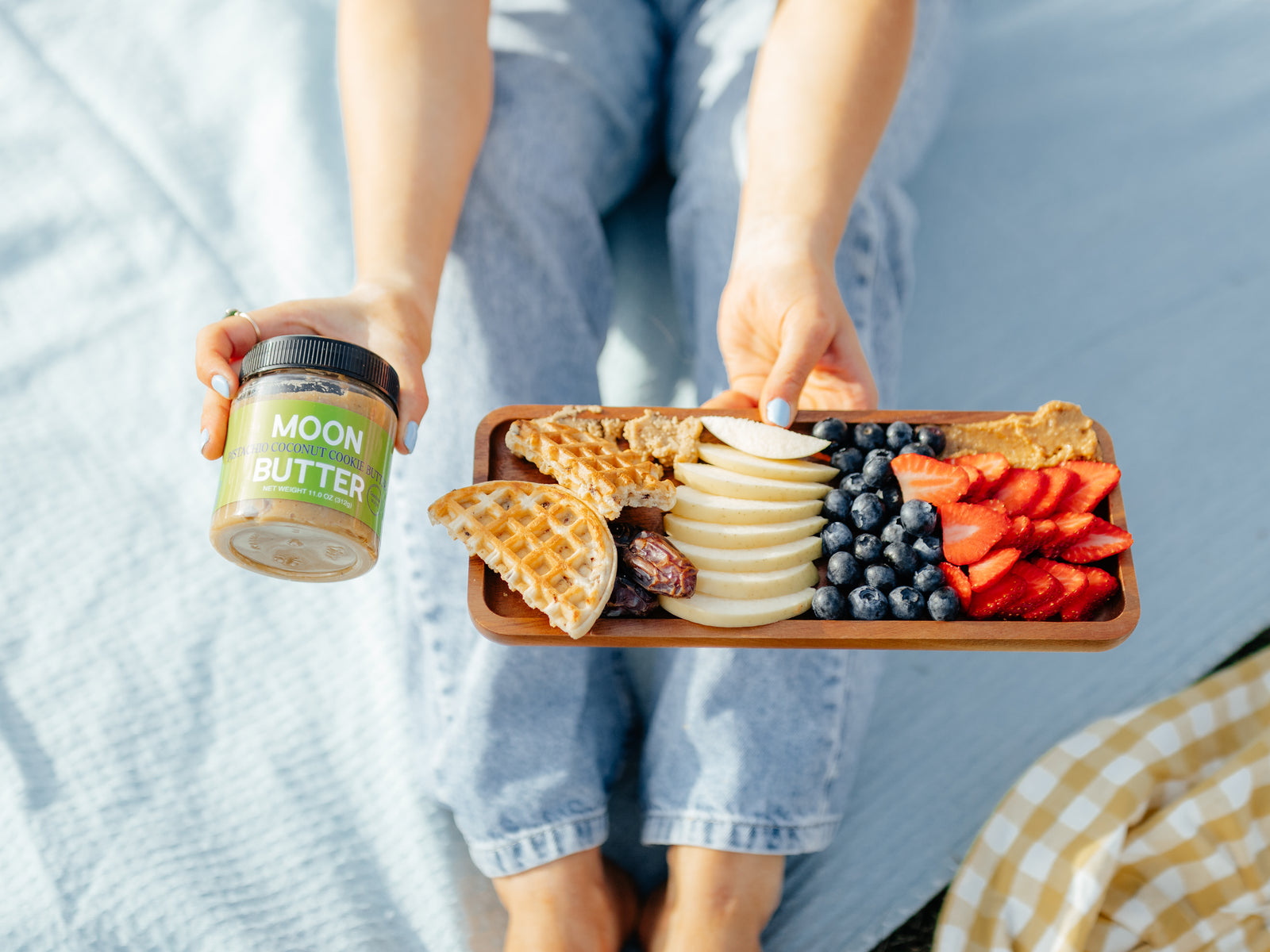 A person holding Moon Butter and a tray of waffles, sliced pears, blueberries, and strawberries