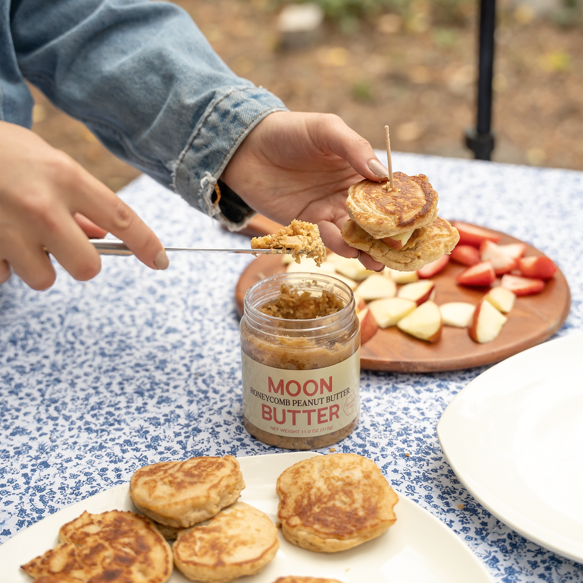 Moon Butter Honeycomb Peanut Butter being spread onto small pancakes beside sliced fruit
