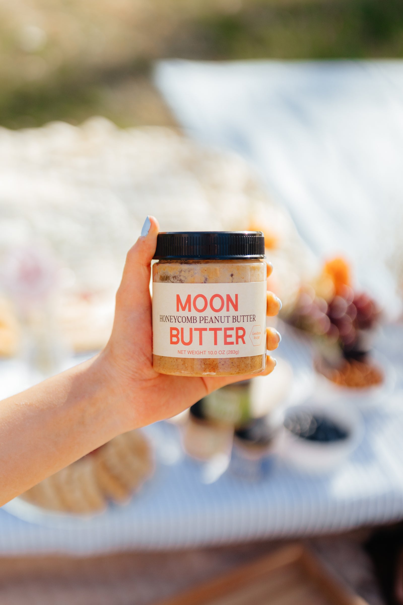 A hand holding a jar of Moon Butter Honeycomb Peanut Butter